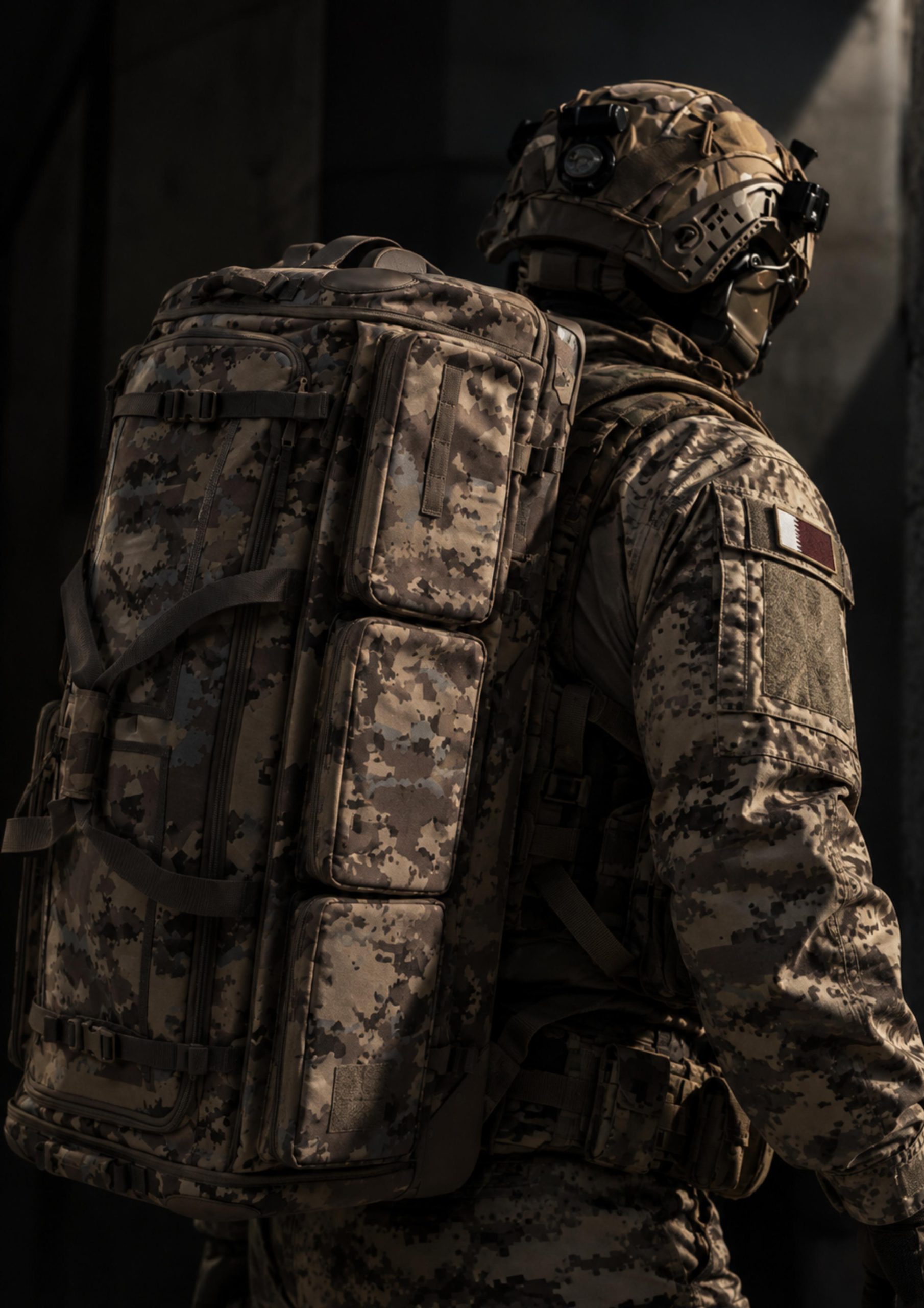 Rear three-quarter view of a person wearing a large camouflage backpack, helmet and uniform with a Qatar flag patch.